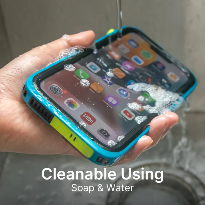 A hand holds an iPhone 13 Pro in a blue and yellow Catalyst Case US Waterproof Case under running water and soap suds. The screen is on with app icons visible. Text at the bottom reads, "Cleanable Using Soap & Water.