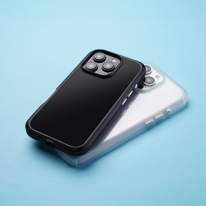 Two smartphones lie on a blue surface; one protected by a Catalyst Drop Proof Case in black, resting on another with a white Catalyst Drop Proof Case, both featuring triple-lens cameras.