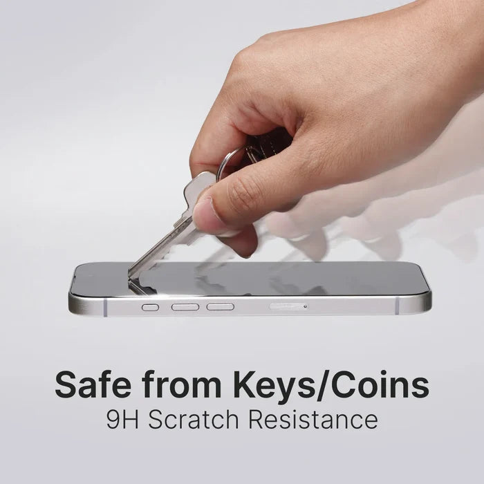 A hand drags a silver key across a smartphone with the Catalyst Case US Tempered Glass Screen Protector, showing its 9H scratch resistance. The phone, with a silver frame, rests on a white surface. Text: “Safe from Keys/Coins.”.