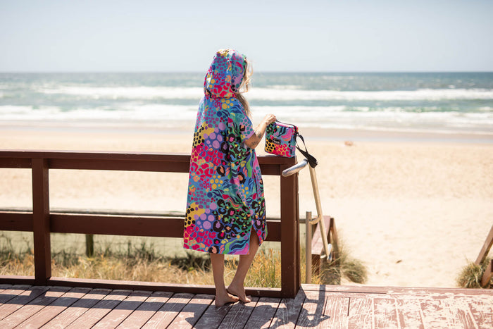 Colorful hooded towel with multicolor circular and floral print, worn by child at beach with matching small bag.