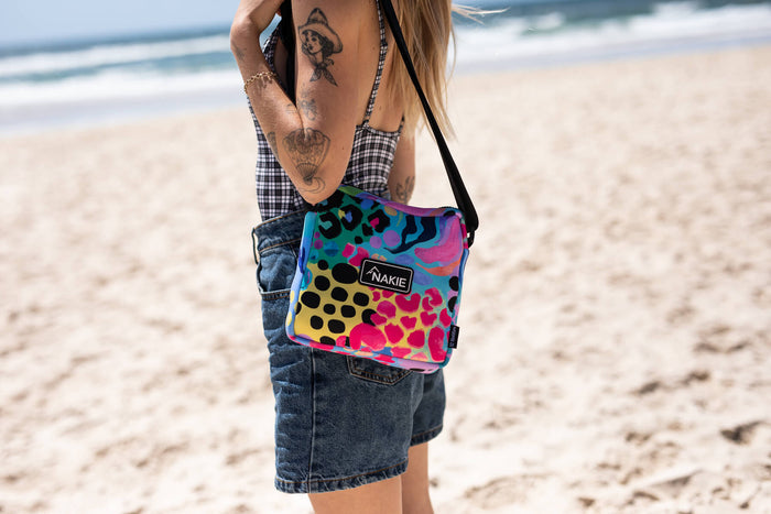 Colorful leopard print hooded towel in rainbow hues with black shoulder strap, worn at beach