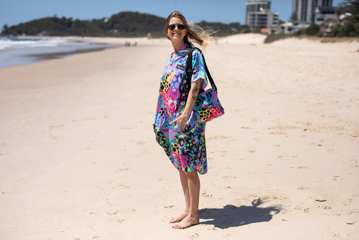 Multicoloured leopard print hooded towel with purple lining, worn on beach over shoulder
