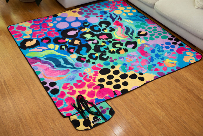Colorful picnic blanket with leopard print, polka dots, wavy patterns, and rainbow colors on blue background, black binding