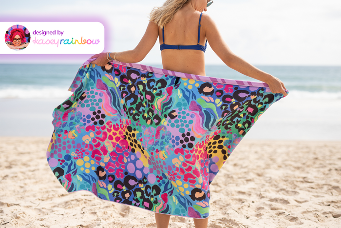 Multicolored recycled sand-free beach towel with leopard and geometric patterns, held open on beach.