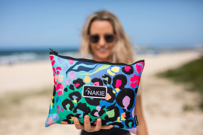 Colorful sand-free beach towel with leopard print and rainbow geometric pattern, rolled and held up at the beach