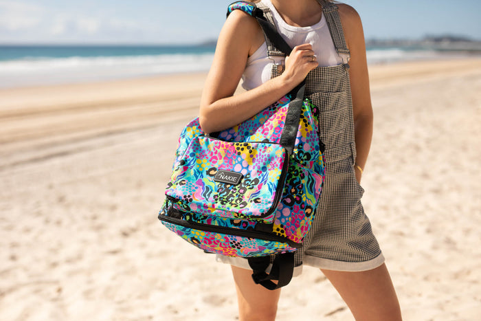 Kasey Rainbow recycled tote bag with multicolour abstract pattern and black trim, worn on shoulder at beach