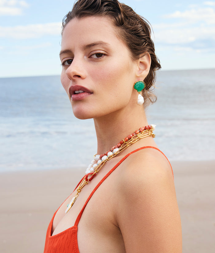 Model on beach wears red swimsuit with Marina Drop Earrings and pearl necklaces