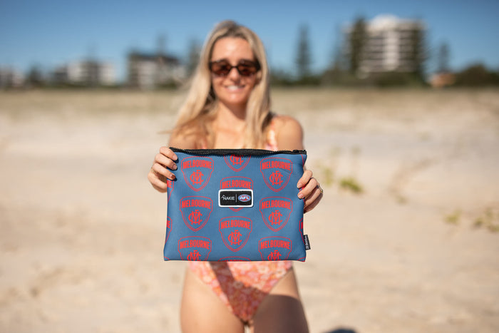 Blue and red Melbourne Demons AFL patterned sand-free beach towel with black zipper, held at the beach