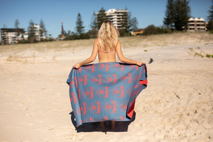 Melbourne Demons AFL recycled beach towel with blue and red circular logo pattern, sand-free material, displayed on beach