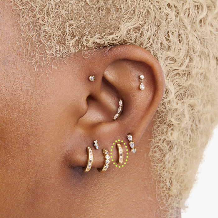 This is an image of a 14K gold plated huggie earring with 4 baguette cut, bezel set crystal CZs along the edge circled on an ear.