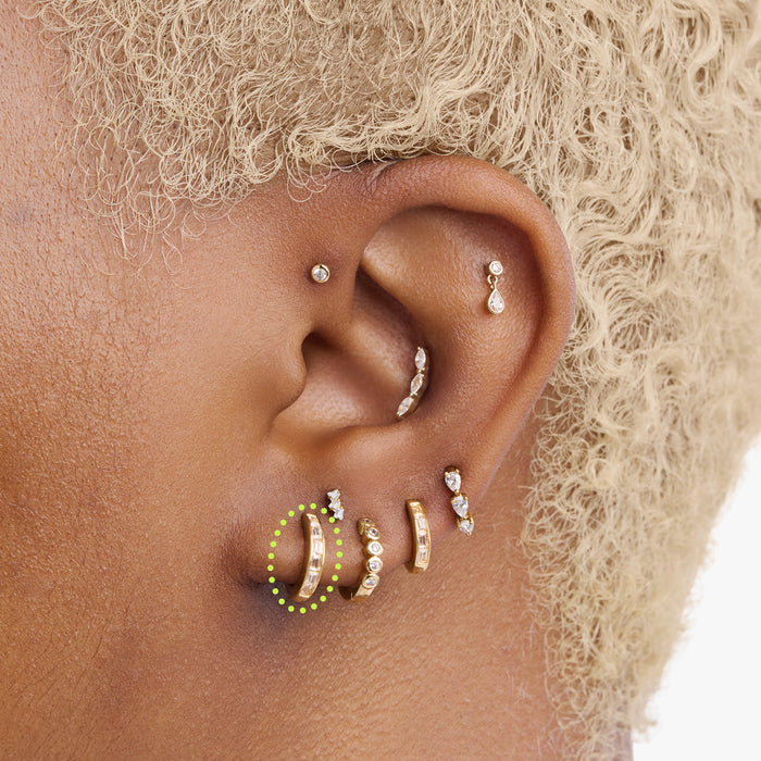This is an image of a 14K gold plated huggie earring with 6 baguette cut, bezel set crystal CZs along the edge circled on an ear.