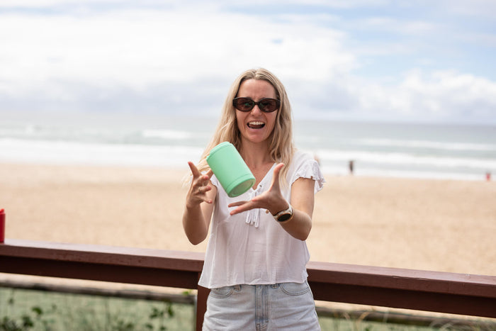 Mint green coffee cup lid displayed by woman on beach boardwalk with ocean background
