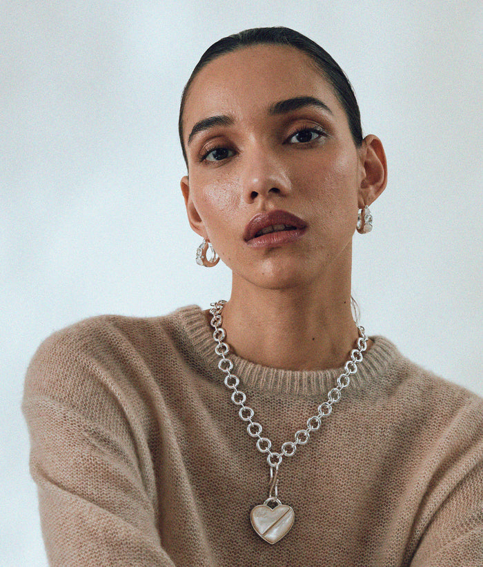 Model in tan sweater wears Mood Necklace and Heart Pendant in Silver, with Piet Hoop Earrings.