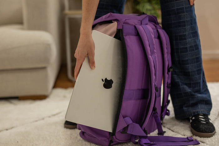Mulberry purple recycled travel backpack with laptop compartment, shown holding silver laptop on person's back.