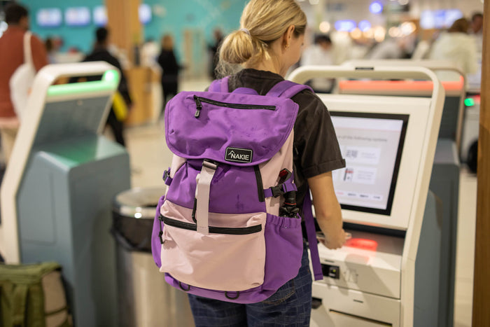 Purple and pink recycled travel backpack with flap closure and front pocket, worn at airport check-in.