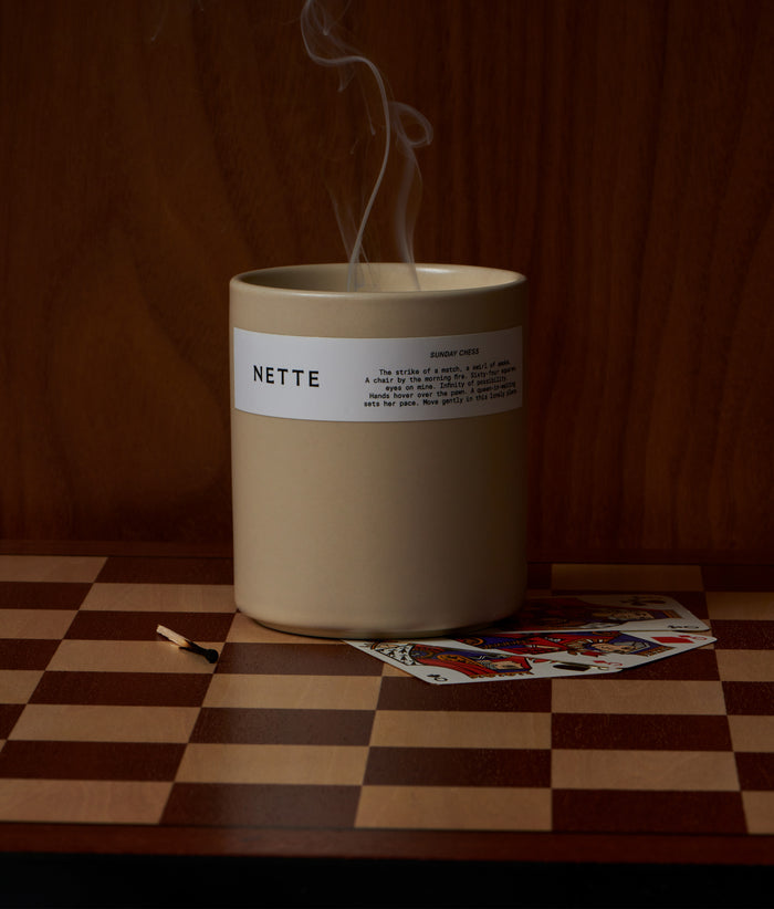 Candle emits smoke, sits on chess board surface with match and playing card.