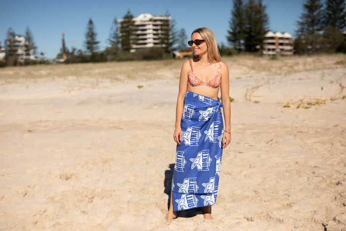 Blue AFL beach towel with white Kangaroos and stadium print, worn as wrap on sand, shown full length.