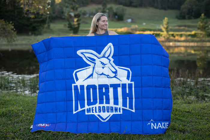 Blue quilted puffy blanket with North Melbourne Kangaroos AFL logo and white kangaroo design, displayed outdoors.