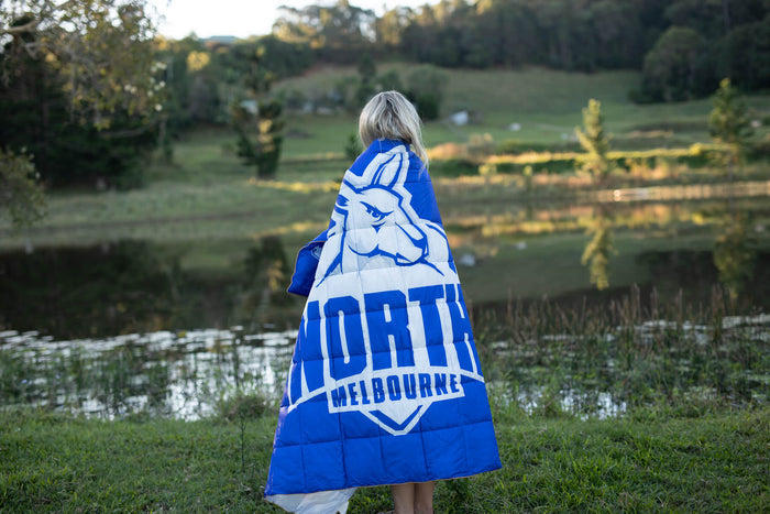 North Melbourne Kangaroos blue and white puffy blanket with team logo, worn as a cape outdoors