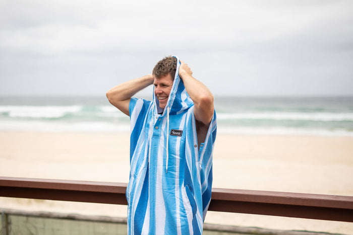 Blue and white striped hooded towel with kangaroo pocket, worn by man at beach
