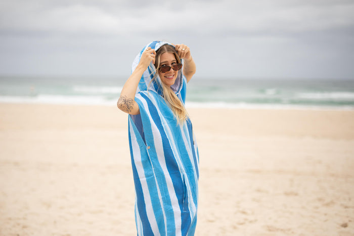 Blue and white striped hooded towel with sand-free texture, worn on beach by woman in sunglasses.