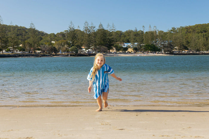 Kids hooded towel in blue and white stripes, worn on beach by child running toward water