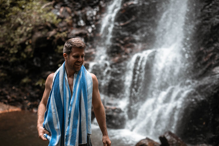 Blue and white striped recycled beach towel draped around man's shoulders near waterfall
