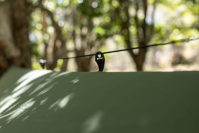 Olive ultralight tarp with black guy line attachment point, forest background.