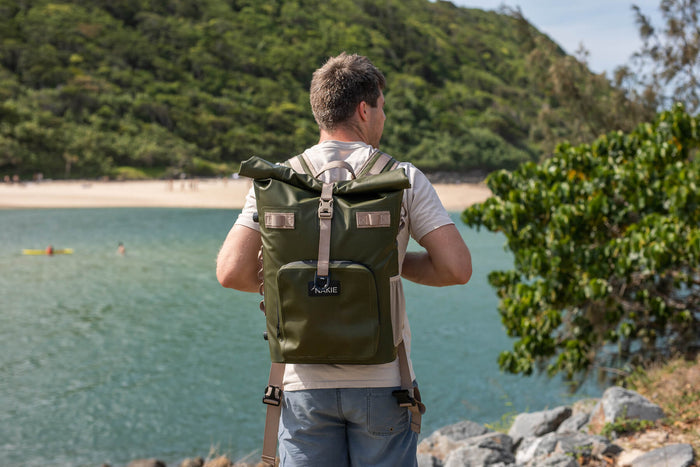 Olive green recycled cooler backpack with roll-top closure and shoulder straps, worn by person overlooking beach.