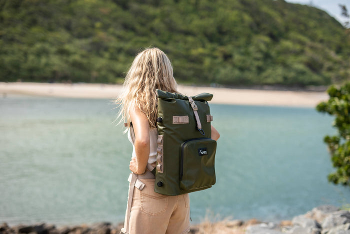 Olive green recycled cooler backpack with roll-top closure, worn by person overlooking beach cove