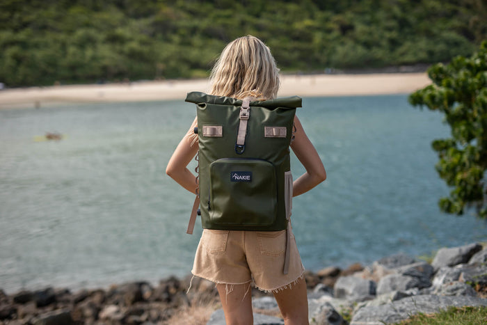 Olive green waterproof cooler backpack with rolled top, front pocket, and dual shoulder straps, worn on beach.