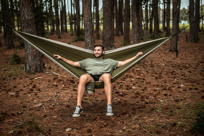 Olive green recycled hammock with black straps suspended between trees, displayed in forest setting