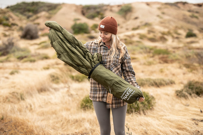 Olive green down puffy blanket rolled and held by person in desert landscape