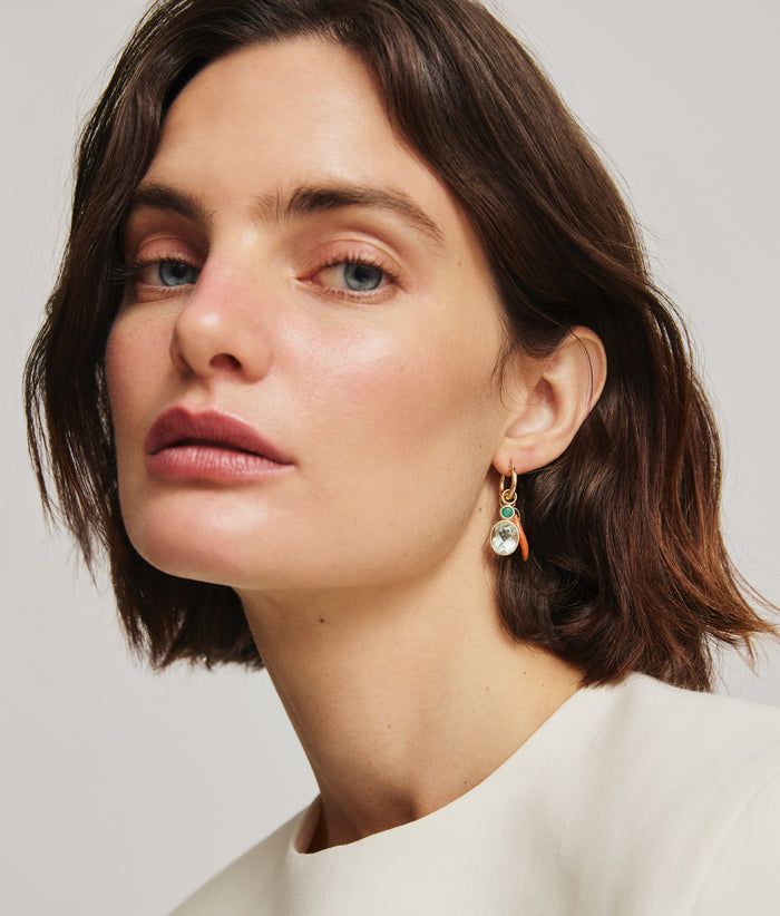 Model wears white top with gold hoop and hanging layered charms in semiprecious oval and coral horn.