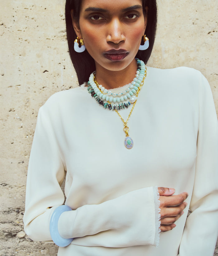 Model in cream dress wears Organic Hoops and Ridge Cuff in Blue Lace with stack of necklaces
