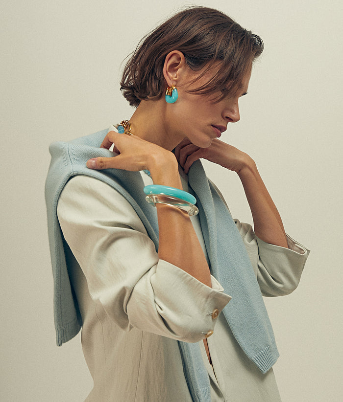 Model with hands on shoulders wears grey blazer and blue sweater with Organic Hoops in Pool and cuff bracelets