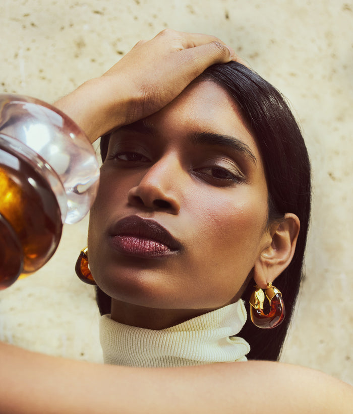 Model on stone backdrop wears Organic Hoops in Tortoise with stack of resin cuffs