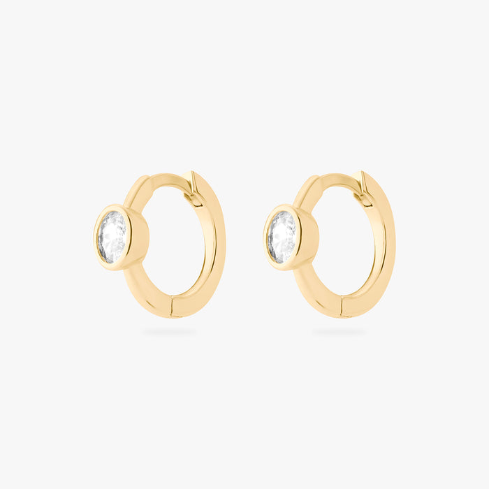 Gold huggie earrings with clear gemstones on a white background