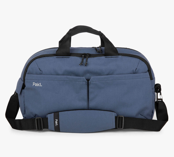 Blue duffel bag with two front zip pockets, padded shoulder strap and black handles; logos read Pakt. and Pakt