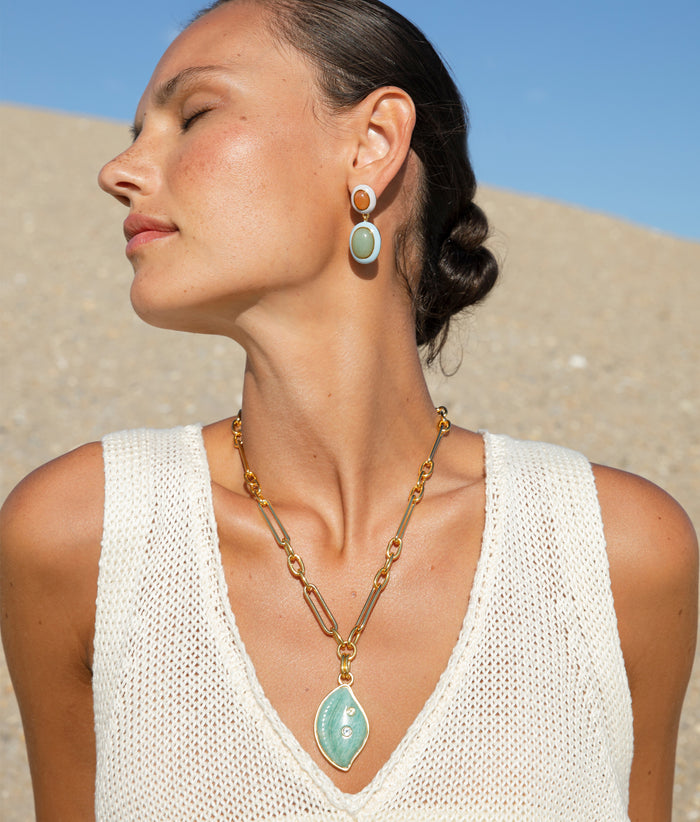 Close up of model on the beach wearing the Papaya Earrings paired with the Cowrie Shell Necklace in Amazonite.