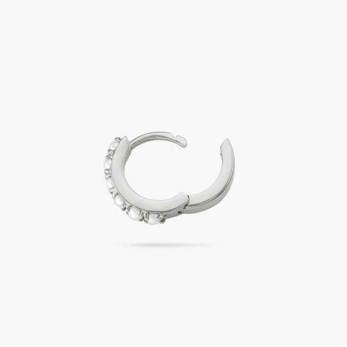 This is a small silver huggie that has small pearls lining the front of it color:null|silver