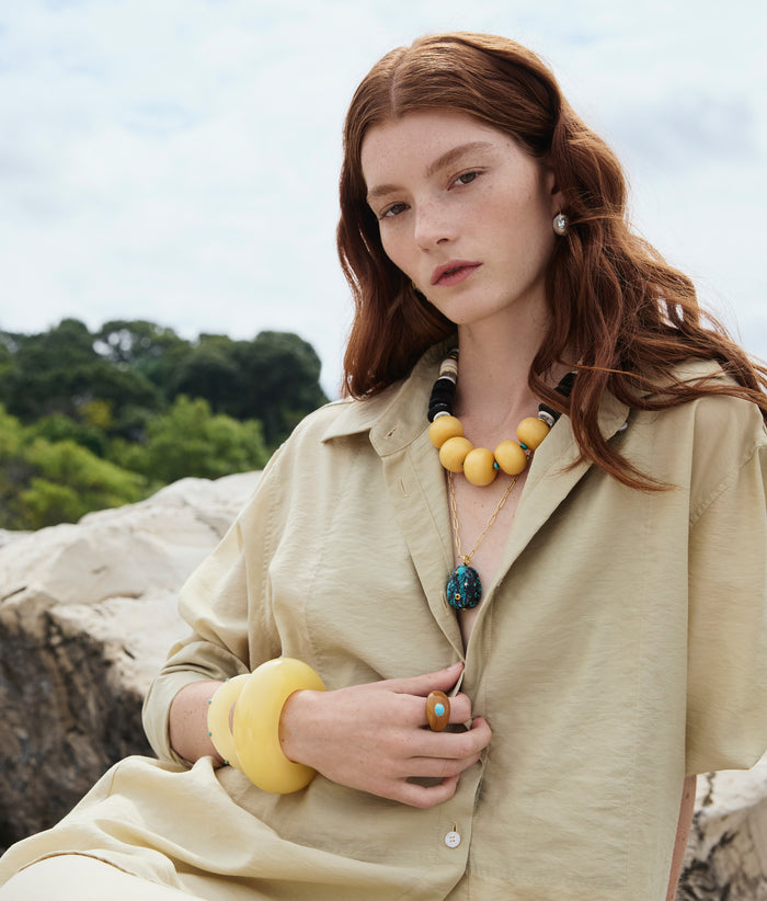 Model wears Pomelo and Manami Necklaces, Monument Ring in Dune, and stack of yellow resin cuffs.