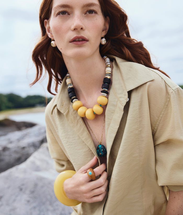 Model holds tan shirt and wears Pomelo and Manami Necklaces, Monument Ring, Pearl Pablo Earrings and Arc Cuff.