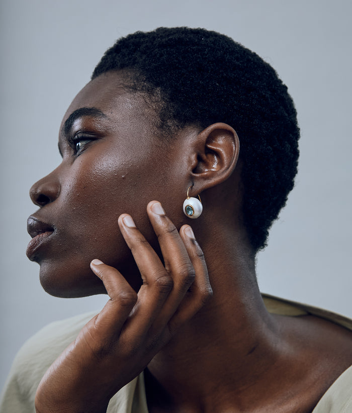 Model against grey background wearing Pearl Pablo Earrings in Blue Topaz