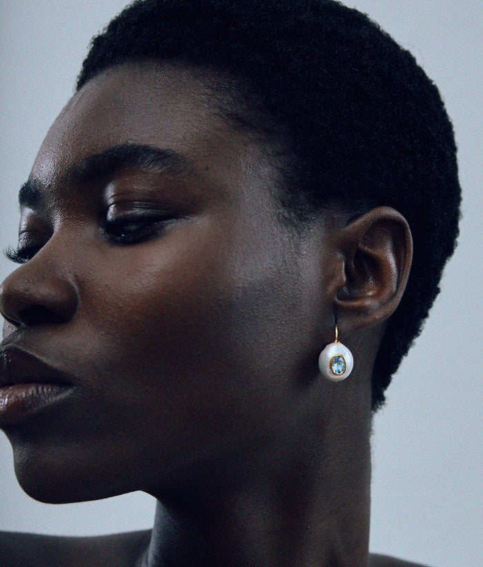 Model against grey background wearing Pearl Pablo Earrings in Blue Topaz