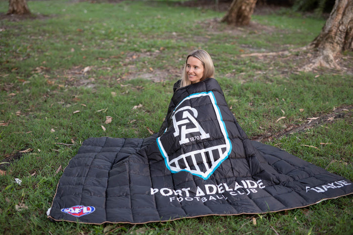 Black quilted stadium blanket with Port Adelaide Power logo, white text, and blue trim, displayed on grass outdoors