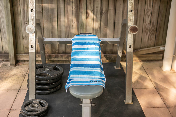 Blue and white striped recycled gym towel draped over weight bench barbell in gym setting
