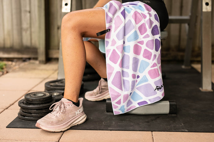 Recycled gym towel with purple, pink, and blue geometric pattern draped over person's leg during workout.