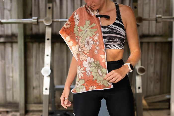 Recycled gym towel in coral with multicoloured floral print, draped over shoulder during workout