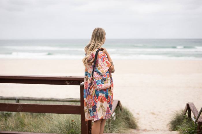 Colorful retro-patterned hooded towel with orange, pink, and blue geometric designs, worn on shoulders at beach.